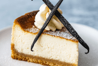 Slice of brown sugar cheesecake with visible vanilla bean specks, glossy brown-butter sheen, and toasted nut garnish on a white plate.