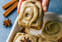 Close-up of chai cinnamon rolls with glossy brown-sugar caramel bottoms and chai cream-cheese frosting, arranged in a rustic baking dish.