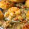 Golden Cheddar Bay biscuit crust crowning creamy shrimp and crab filling with peas and carrots in a white pie dish.