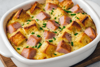 Eggs Benedict casserole in a baking dish with golden muffin cubes, Canadian bacon, and hollandaise sauce — a Best Easy Breakfast Casserole that works as a Summer Brunch Dish, Breakfast For Dinner For A Crowd, or thoughtful Food For A Wake. Perfect Shareable Breakfast Dishes, easy Egg Bake Ideas, and versatile Make Ahead Brunch Dishes for holidays, gatherings, or casual Brunch Ideas For Two People.