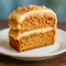 Slice of applesauce spice cake topped with cinnamon cream cheese frosting and chopped pecans on a ceramic plate.