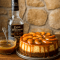 Close-up of a slice of roasted-peach bourbon cheesecake with a pecan-graham crust, glossy caramel drizzle, and peach slices on top — a showy Super Bowl Cheesecake idea, nodding to an Andies Candies Cheesecake vibe, and a great pin for Fruity Cheesecake Recipes.