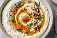 Bowl of whipped ricotta topped with hot honey drizzle, chopped walnuts, and rosemary, surrounded by toasted bread slices – perfect Pre Dinner Snack Ideas and easy Snacks To Bring To A Gathering for Girls Day Food, Fun Appetizers To Make, and casual Hosting Appetizers Entertaining or Meals For Party. Great as Hors D’oeuvres Ideas Easy, trendy East Coast Appetizers, or delicious Tapas Appetizers.