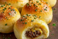 Golden-brown garlic Parmesan cheeseburger bombs on a platter, each one oozing melted cheddar with a sprinkle of grated Parmesan and chopped parsley, served with a bowl of dipping sauce.