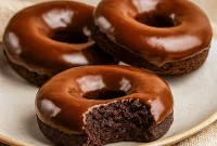 Close-up of three glazed chocolate protein donuts on parchment with almond crumbs — a perfect visual for Healthy Sweet Protein Snacks, and a tempting idea for a Protein Air Fryer Dessert. This shot also reads as Gluten Free Paleo Desserts and Healthy Non Dairy Desserts, with a decadent Health Chocolate Desserts vibe; great for Dairy Free Healthy Meals, Healthy Gluten Free Baking Recipes, labeled as Macros Desserts and useful inspiration for Protein Powder Meals.