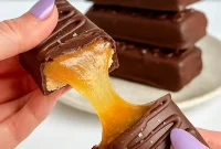 Close-up of gluten-free protein Twix bars: almond shortbread base, gooey nut-butter caramel, and glossy dark chocolate coating with a sprinkle of sea salt.