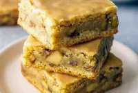 Close-up of a maple-glazed apple blondie square with tender apple bits and a glossy maple drizzle on parchment paper.