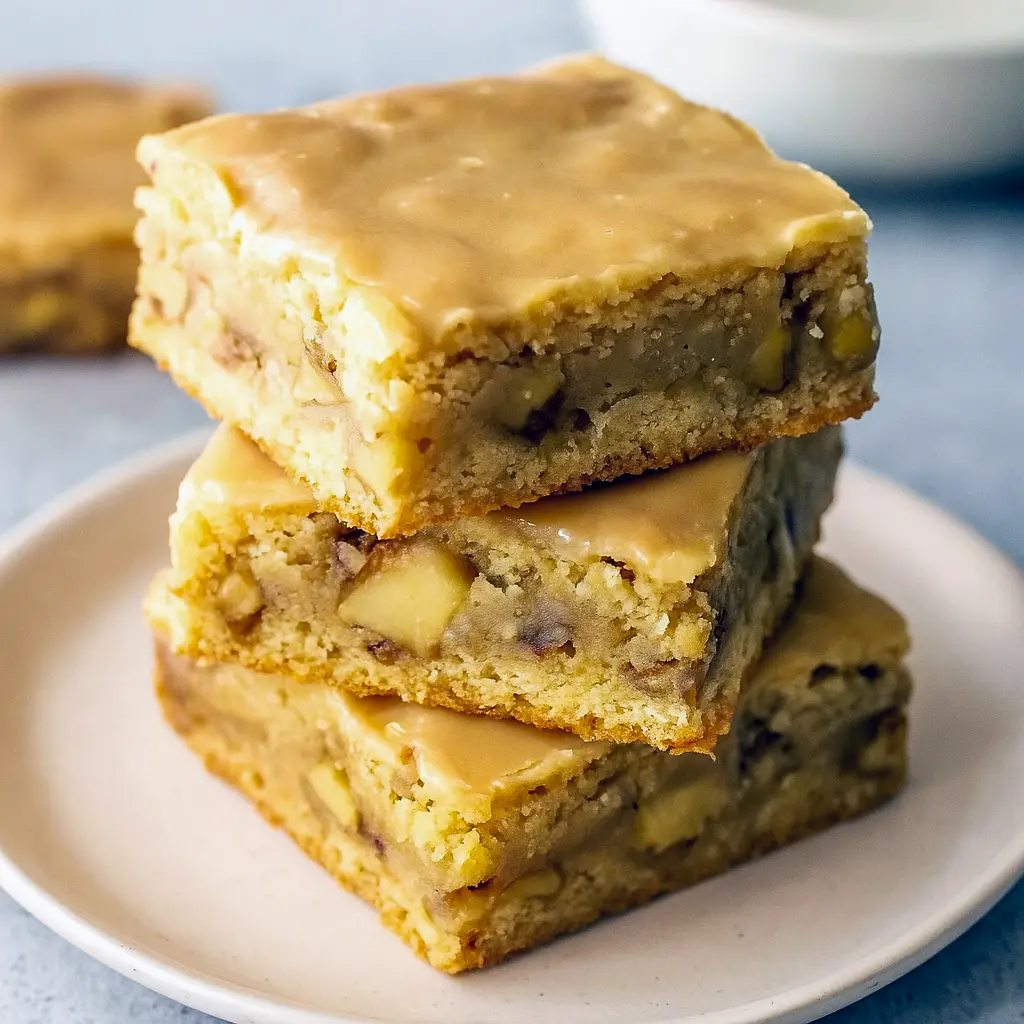 Close-up of a maple-glazed apple blondie square with tender apple bits and a glossy maple drizzle on parchment paper.