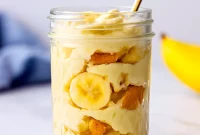 Close-up of a jar showing stacked protein banana pudding, crushed wafers, and banana slices — a tasty idea for Things To Add Protein Powder To and a clean Vanilla Protein Dessert Recipes option; great as Soft Foods With Protein and tested with Ascent Protein Recipes.