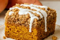 Overhead slice of pumpkin coffee cake with thick streusel topping and drizzle of glaze on a white plate.