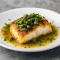Pan-seared cod piccata with lemon-caper glaze and parsley on a white plate.