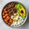 Overhead shot of a bowl with seasoned ground beef, roasted sweet potato cubes, sliced avocado, dollops of cottage cheese, and a honey drizzle, garnished with cilantro.