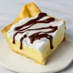 Golden cream puff cake with airy layers, silky vanilla filling, and a rich chocolate drizzle on a cozy autumn table setting, a Must Try Desserts.