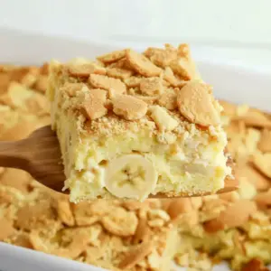 Golden banana blondie squares topped with sliced bananas and crushed vanilla wafers on a serving plate.