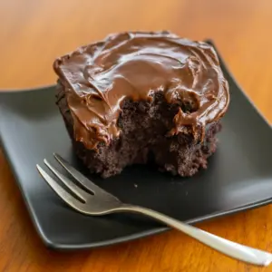 Fudgy chocolate mug cake in a white mug, spoon scooping a warm, gooey center (topped with a small dollop of whipped cream).