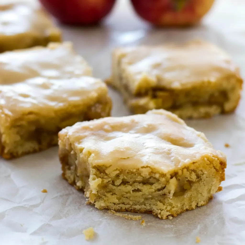 Golden-brown blondie squares dotted with tender apple pieces, drizzled with glossy maple glaze and dusted with cinnamon — a warm, fall dessert ready to serve, Fall Blondies Recipe.