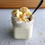 Close-up of a mason jar filled with layered Banana Cream Pie Overnight Oats, showing creamy yogurt and mashed banana with a graham cracker crumble — a dreamy Overnight Oatmeal With Yogurt that's an Overnight Oats Recipe Easy to prep and a serious candidate for the Best Overnight Oats Recipe; styled as one of my favorite Oat Recipes Healthy and an Overnight Oats Recipe Healthy grab-and-go Overnight Oatmeal, inspired by Banana Cream Pie and perfect for Breakfast Meal Prep.