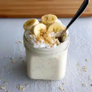 Close-up of a mason jar filled with layered Banana Cream Pie Overnight Oats, showing creamy yogurt and mashed banana with a graham cracker crumble — a dreamy Overnight Oatmeal With Yogurt that's an Overnight Oats Recipe Easy to prep and a serious candidate for the Best Overnight Oats Recipe; styled as one of my favorite Oat Recipes Healthy and an Overnight Oats Recipe Healthy grab-and-go Overnight Oatmeal, inspired by Banana Cream Pie and perfect for Breakfast Meal Prep.