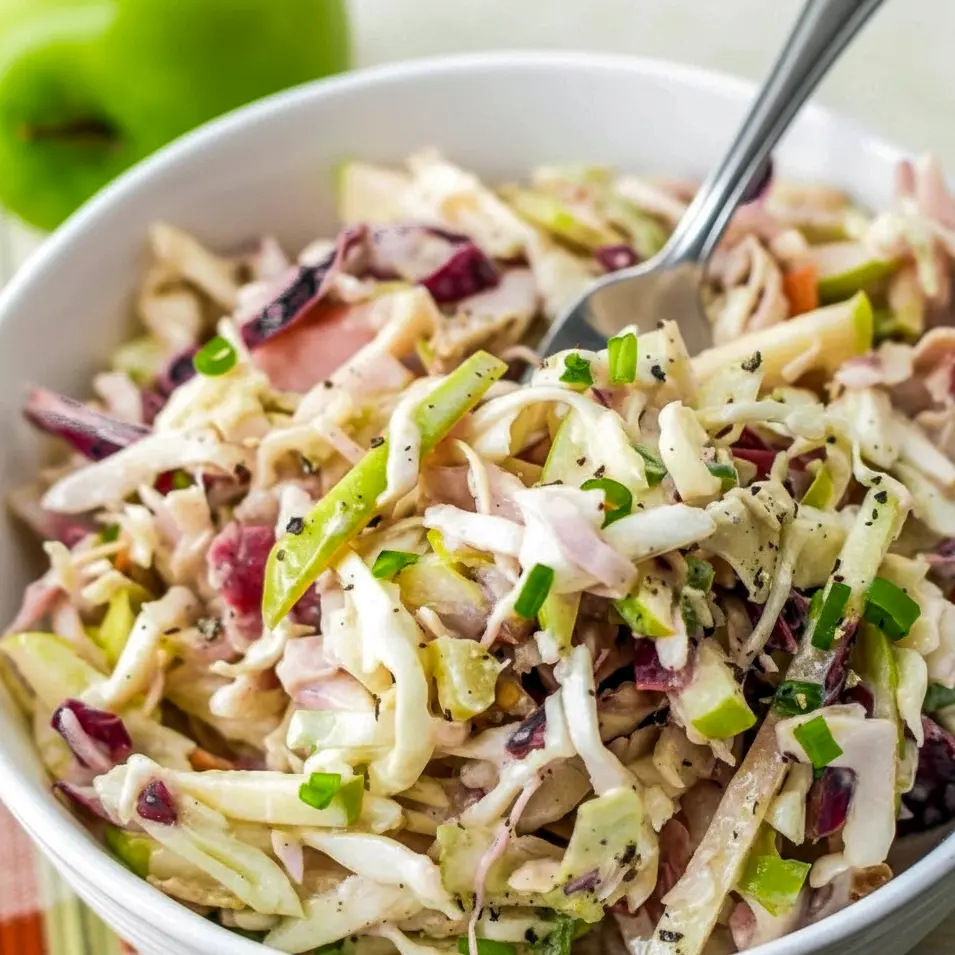 Close-up of a white bowl filled with crisp apple coleslaw: shredded cabbage, matchstick apples, celery, and green onions tossed in a warm apple-cider dressing, ready for serving, Apples In Salad.