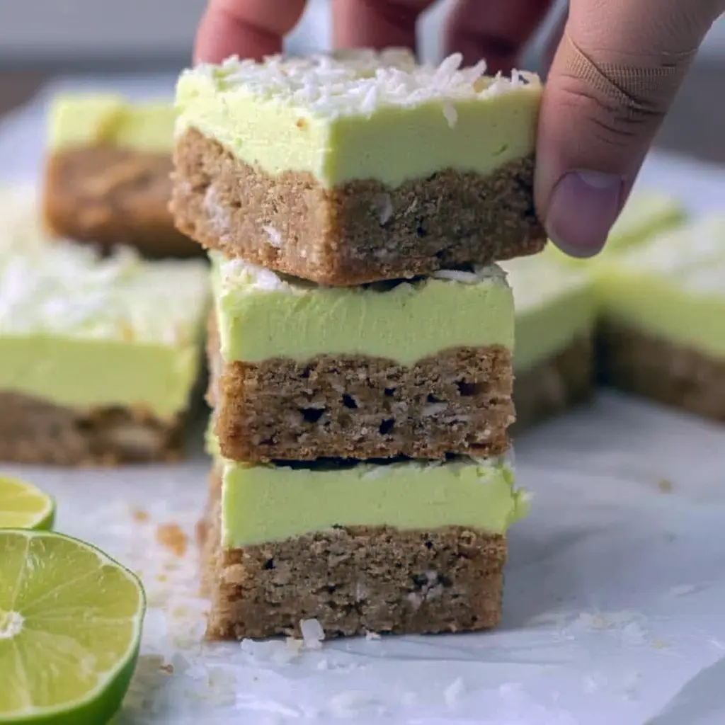 Squares of lime-frosted coconut bars with shredded coconut and a white chocolate drizzle on a festive serving board, Starbucks Bars.