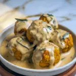 Close-up of golden-browned pumpkin chicken meatballs sitting in a glossy sage cream sauce, garnished with fresh sage leaves on a rustic plate, Homemade Fall Recipes.