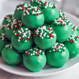 Close-up of glossy green truffles coated in candy melts with festive sprinkles; one truffle is cut open to reveal a creamy chocolate-cookie center, Christmas Truffles.