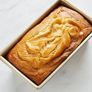 Sliced golden loaf revealing a creamy cheesecake swirl and caramel ribbons, drizzled with glossy caramel — warm breakfast or dessert loaf, Quick Caramel Cream Cheese Bread.
