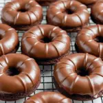 Chocolate protein donut with a glossy glaze and a light dusting of cocoa, stacked on a cooling rack, High Protein Baked Donuts.