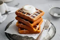Stack of golden Best Gingerbread Waffles topped with whipped cream and syrup, styled for a cozy Christmas Breakfast Waffles spread.