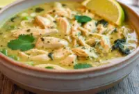 Bowl of Thai Ginger Chicken Soup with shredded chicken, sliced bell pepper, spinach, cilantro, and a lime wedge.