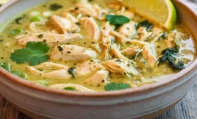 Bowl of Thai Ginger Chicken Soup with shredded chicken, sliced bell pepper, spinach, cilantro, and a lime wedge.