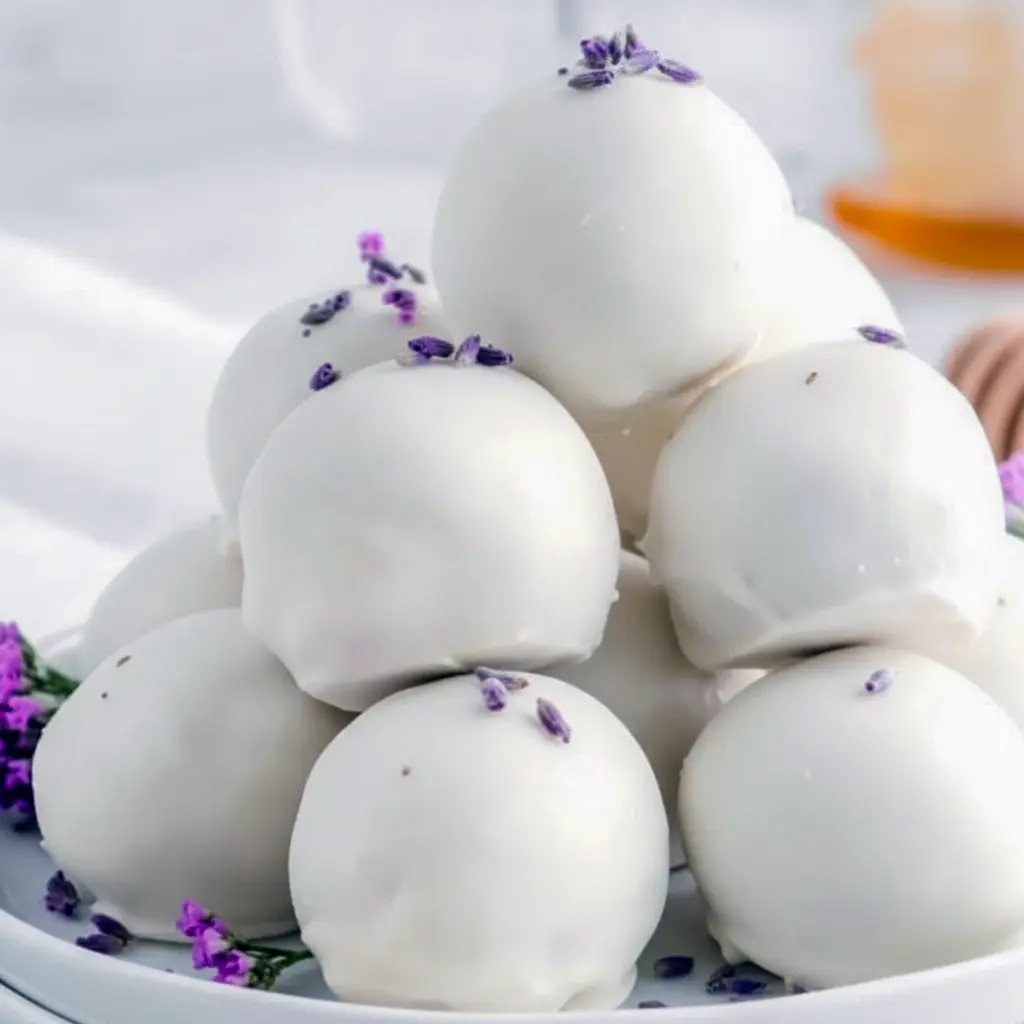 Close-up of glossy white chocolate Chocolate Truffles dusted with dried lavender and a light honey drizzle, arranged on parchment for a delicate spring dessert.