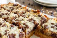 Magic Cookie Bars stacked on a plate, showing gooey chocolate chips, toasted coconut, and chopped nuts.