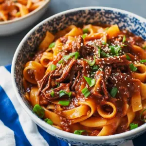 Steaming bowl of glossy shredded beef tossed with udon noodles, topped with sesame seeds and fresh cilantro, Korean Beef Noodles Recipe.
