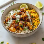 Overhead shot of a Street Corn Chicken Rice Bowl: sliced seasoned chicken thighs on a bed of fluffy white rice, charred corn mixed with creamy sauce and crumbled Cotija, garnished with cilantro, avocado slices, and a lime wedge, Quick Fresh Dinner Ideas.