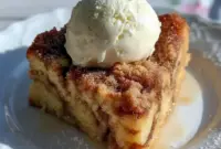 Slice of Eggnog Bread Pudding with a golden cinnamon-sugar top, gooey brioche center, and a generous drizzle of warm eggnog sauce, dusted with nutmeg.