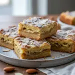 Close-up of golden blondie squares with swirled almond frangipane, toasted sliced almonds, and a light dusting of powdered sugar, Almond Croissant.