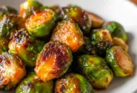 Close-up of Maple Glazed Brussel Sprouts with glossy caramelized edges and orange zest on a rustic serving plate.