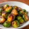 Close-up of Maple Glazed Brussel Sprouts with glossy caramelized edges and orange zest on a rustic serving plate.