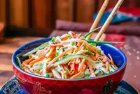 Close-up bowl of Kani Salad Recipe with shredded crab sticks, julienned cucumber and carrot, creamy spicy mayo dressing, and sesame seeds — a vibrant, chilled Japanese-style salad.