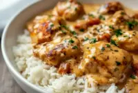 Smothered Chicken And Rice Dinner — close-up of golden chicken thighs nestled in a creamy mushroom-onion gravy over fluffy rice, garnished with chopped parsley (Homestyle Chicken And Rice Casserole).