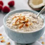 Jar of creamy coconut overnight oats topped with whipped cream, banana slices, and toasted shredded coconut, Creamy Oats With Coconut Milk.