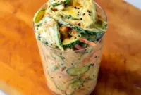 Jar of Creamy Asian Cucumber Salad showing thin cucumber slices, shredded carrots, edamame, tofu, and sesame seeds — a fresh, portable bowl ideal for Easy Light Dinners For Two.