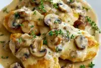 Mushroom Asiago Chicken Recipe — skillet of tender chicken in a creamy Asiago-mushroom sauce, garnished with thyme and grated cheese.