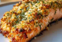 Parmesan-Crusted Salmon on a plate with lemon wedges and greens — golden crust and flaky fish, a classic Salmon Dinner Idea.
