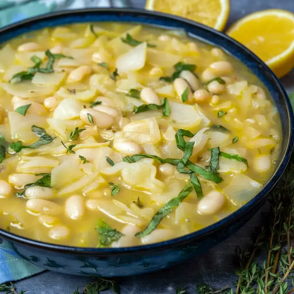 Bowl of steaming Bean And Cabbage Soup with shredded cabbage, white beans, fresh basil, and a lemon wedge, served with crusty bread.