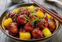 Plate of Pineapple Chicken glazed with brown-sugar sauce and pineapple chunks, garnished with green onions and served over rice.