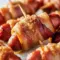 Smokies Recipe close-up: skewered bacon-wrapped little smokies glazed with brown sugar, piled on a platter next to a small bowl of Appetizer Dips.