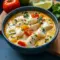 Fish Stew With Coconut Milk: creamy coconut broth with chunks of white fish, chopped cilantro, and a lime wedge, served in a shallow bowl.
