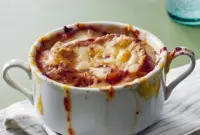 French Onion Soup Recipe — steaming bowl of onion soup topped with a toasted baguette slice and bubbling, browned cheese under the broiler.